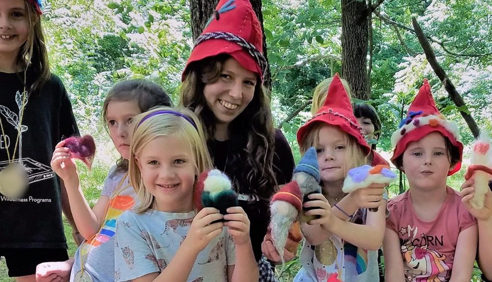 Smiling children in red felt gnome hats holding felted gnomes