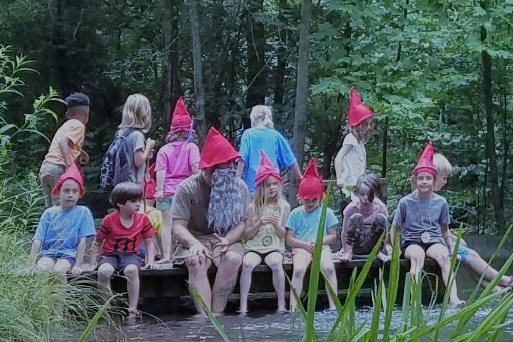 Children in red gnome hats sitting together on a dock by the creek