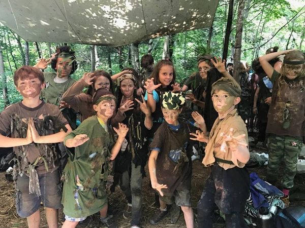 Forest Ninja campers with mud-painted faces under a tarp in the woods