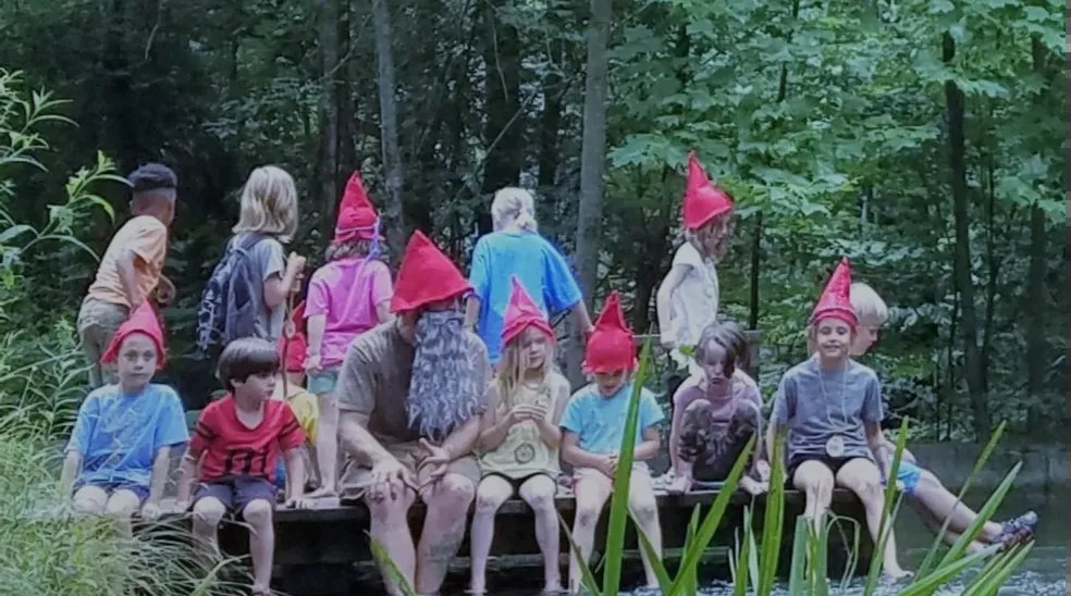 Children in red gnome hats on a log bridge in the forest